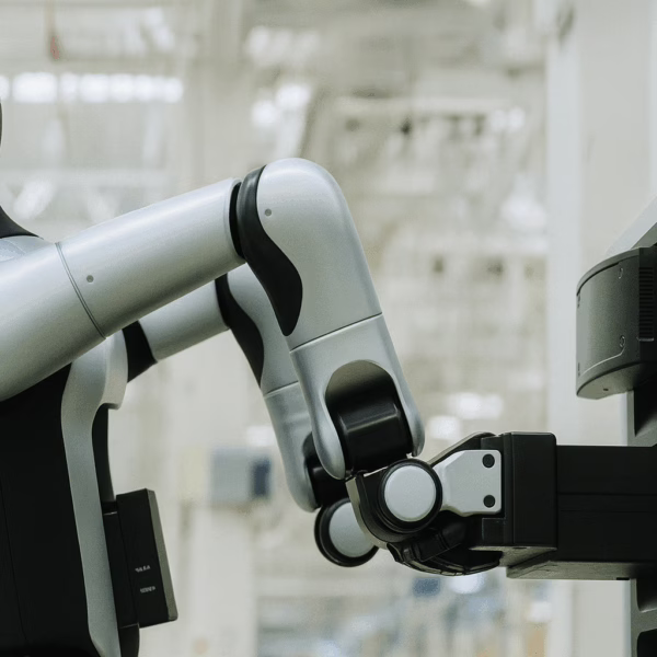 A humanoid robot in a factory carefully inserts a rectangular battery pack into a charging station, demonstrating autonomous battery swapping technology.