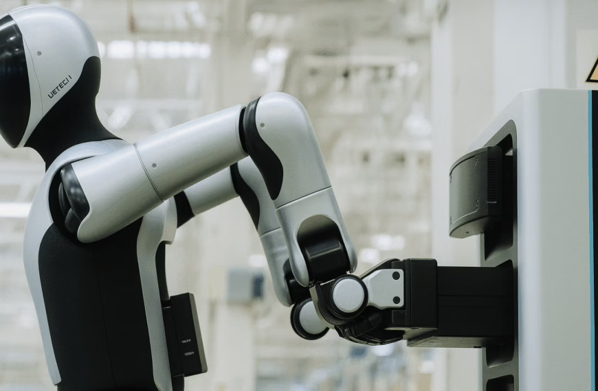 A humanoid robot in a factory carefully inserts a rectangular battery pack into a charging station, demonstrating autonomous battery swapping technology.