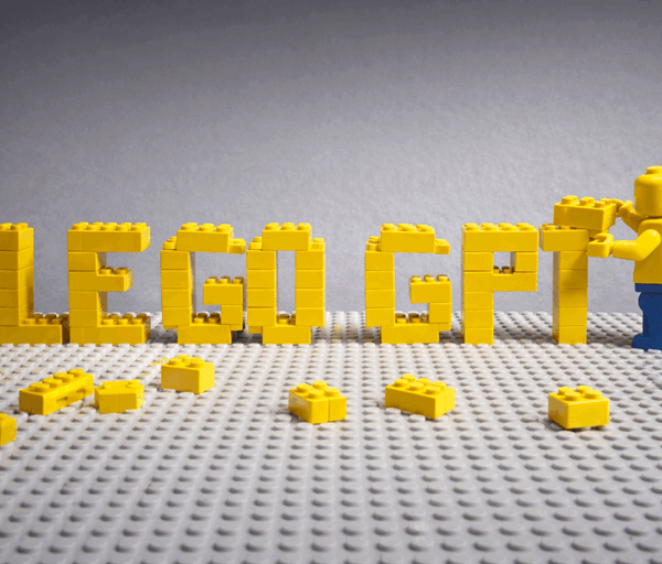 Photo realistic Lego scene showing Lego GPT spelled in yellow bricks as a humanoid figure places the final block on a baseplate.
