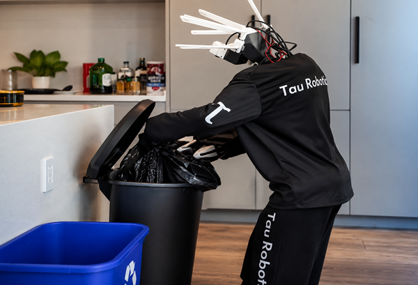 Humanoid robot from Tau Robotics places a rubbish bag into a kitchen bin during a home cleaning demonstration in California.