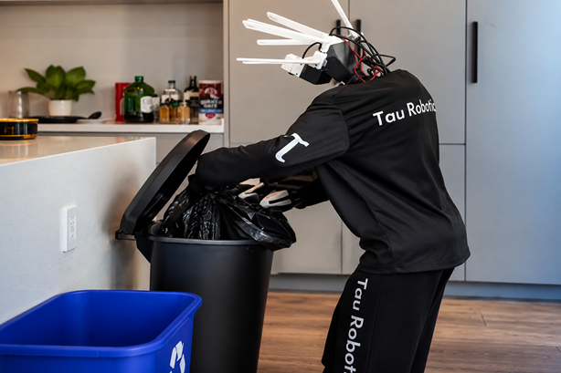 Humanoid robot from Tau Robotics places a rubbish bag into a kitchen bin during a home cleaning demonstration in California.