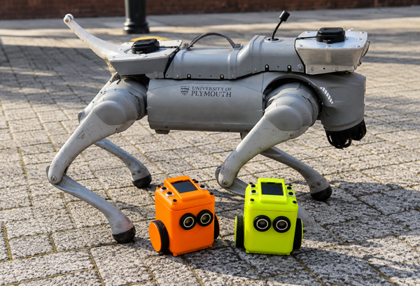 Two Tinkibots stood by a robot dog.