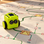 Lime green robot with two circular sensors follows winding green lines across an electronic schematic illuminated by warm golden sunlight.